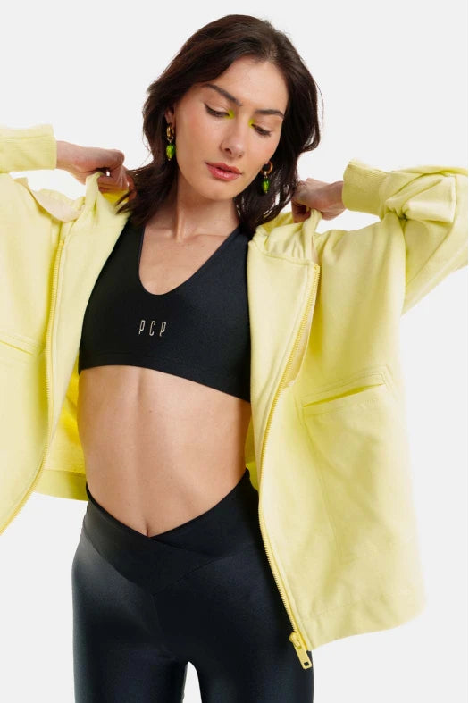 Woman wearing a black sports bra and leggings with a yellow jacket on a white background