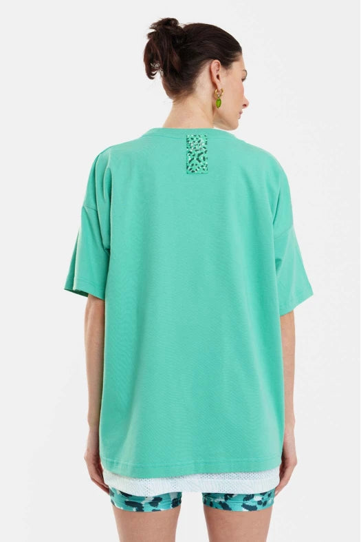 Person wearing a teal t-shirt with a pattern on the back, standing against a white background