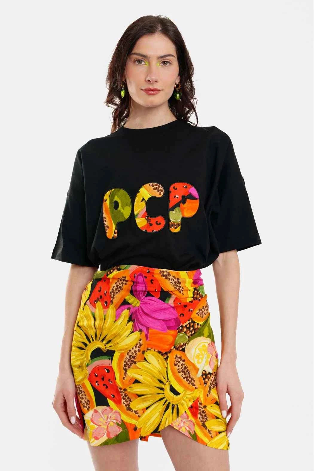 Woman wearing a black t-shirt with colorful text and a vibrant floral skirt on a white background