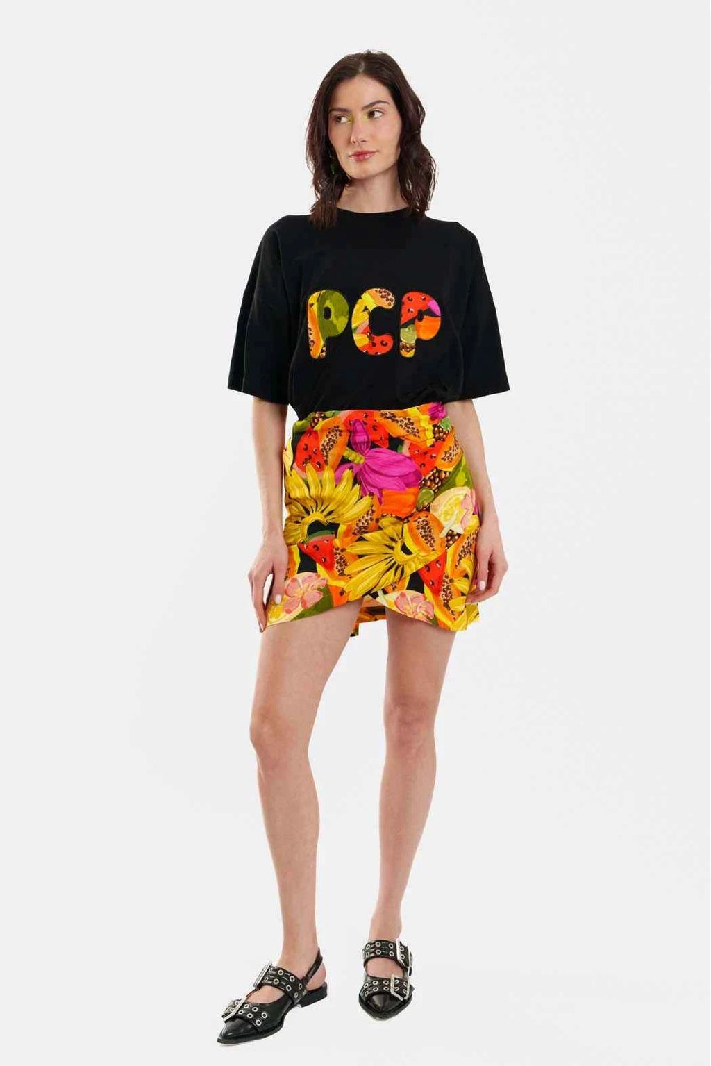 Woman wearing a black t-shirt with colorful text and a floral skirt on a white background