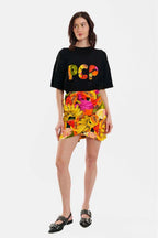 Woman wearing a black t-shirt with colorful text and a floral skirt on a white background