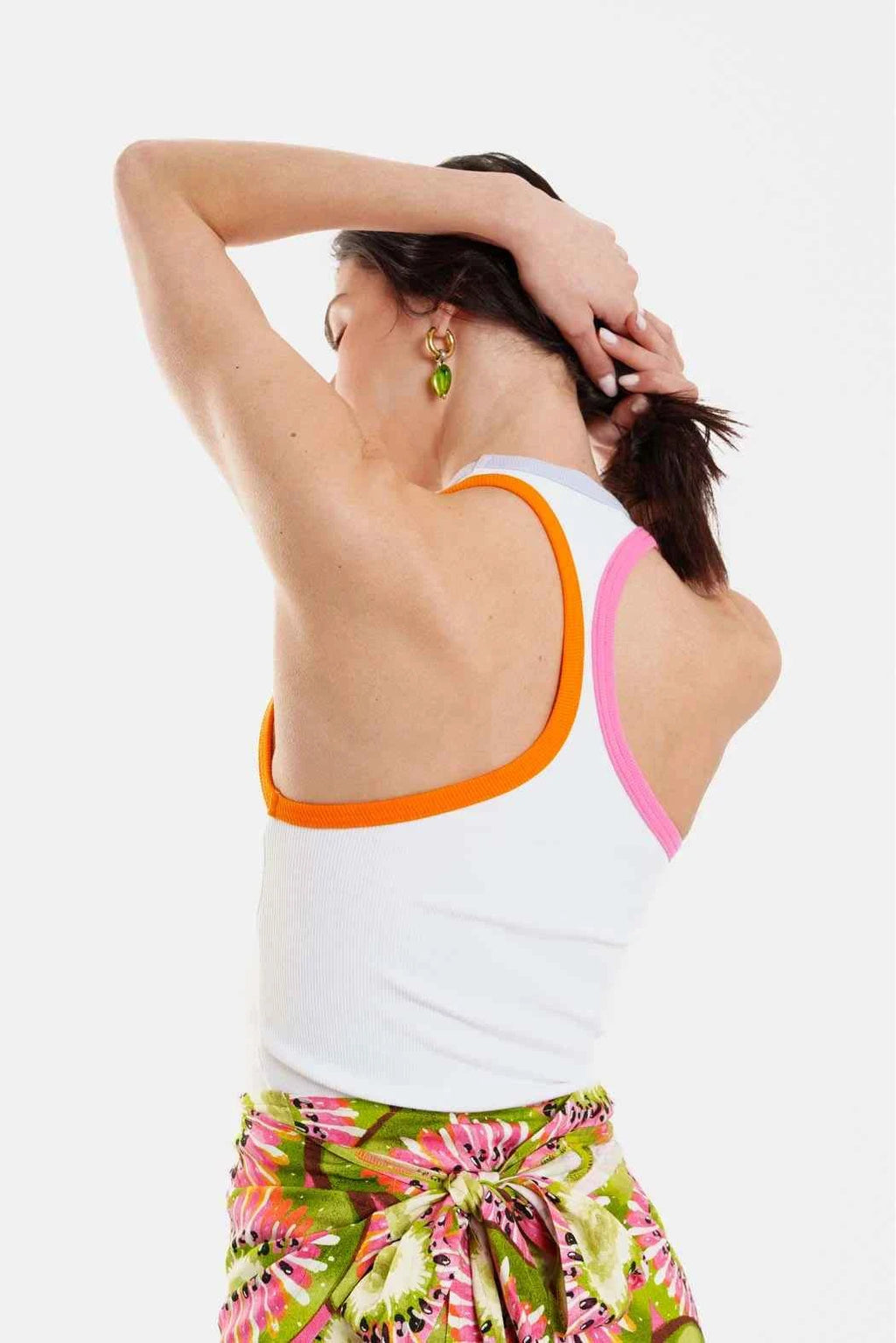 Woman wearing a white tank top with orange trim and colorful pants on a white background