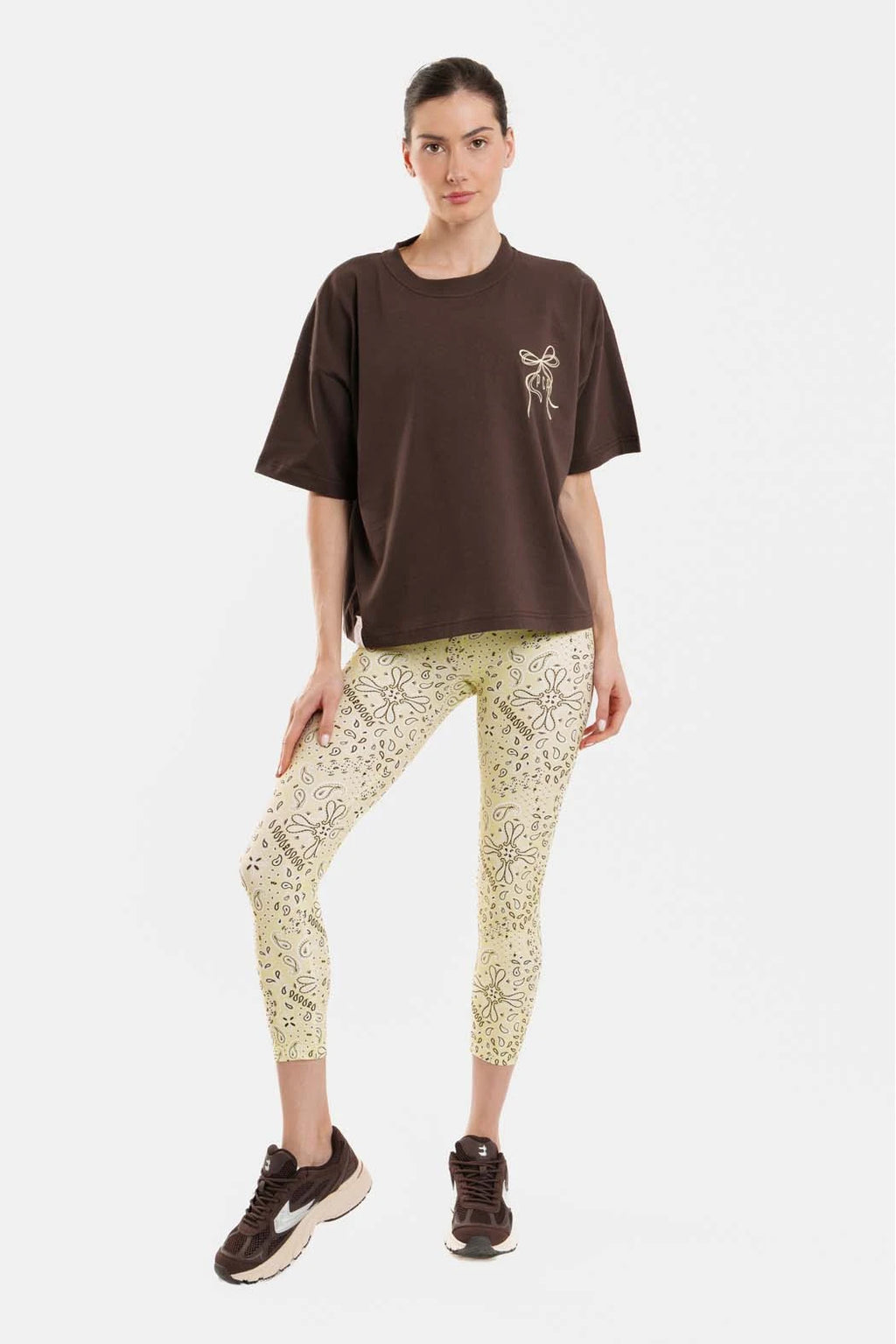 Person wearing a brown t-shirt with a logo and patterned leggings on a white background
