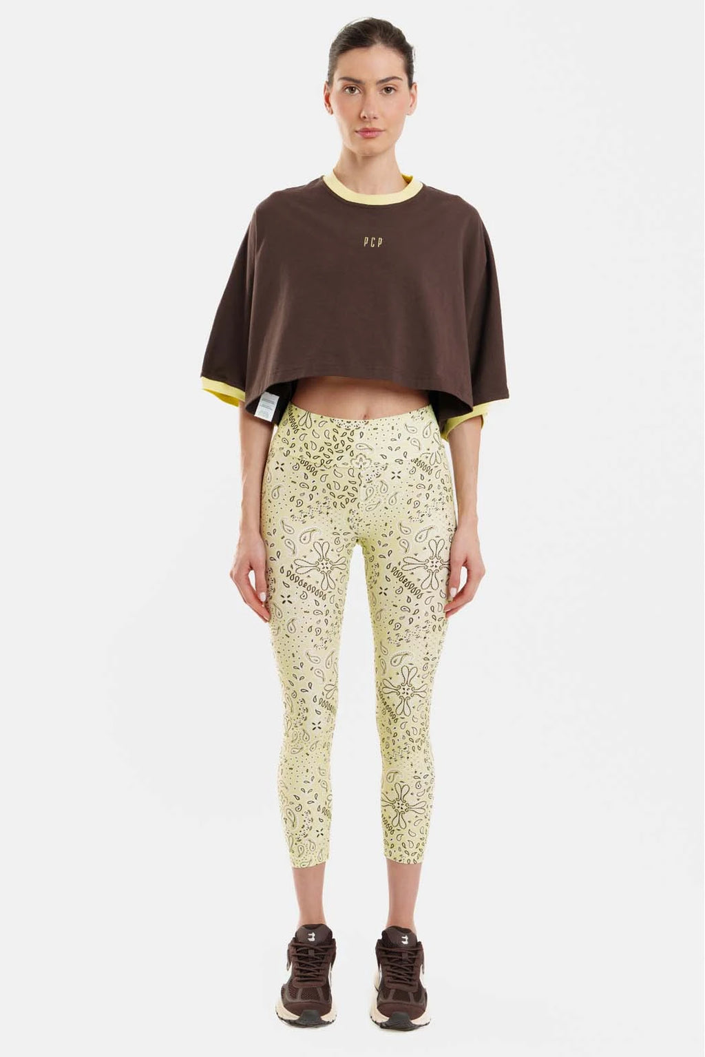 Person wearing a brown cropped top and patterned leggings on a white background