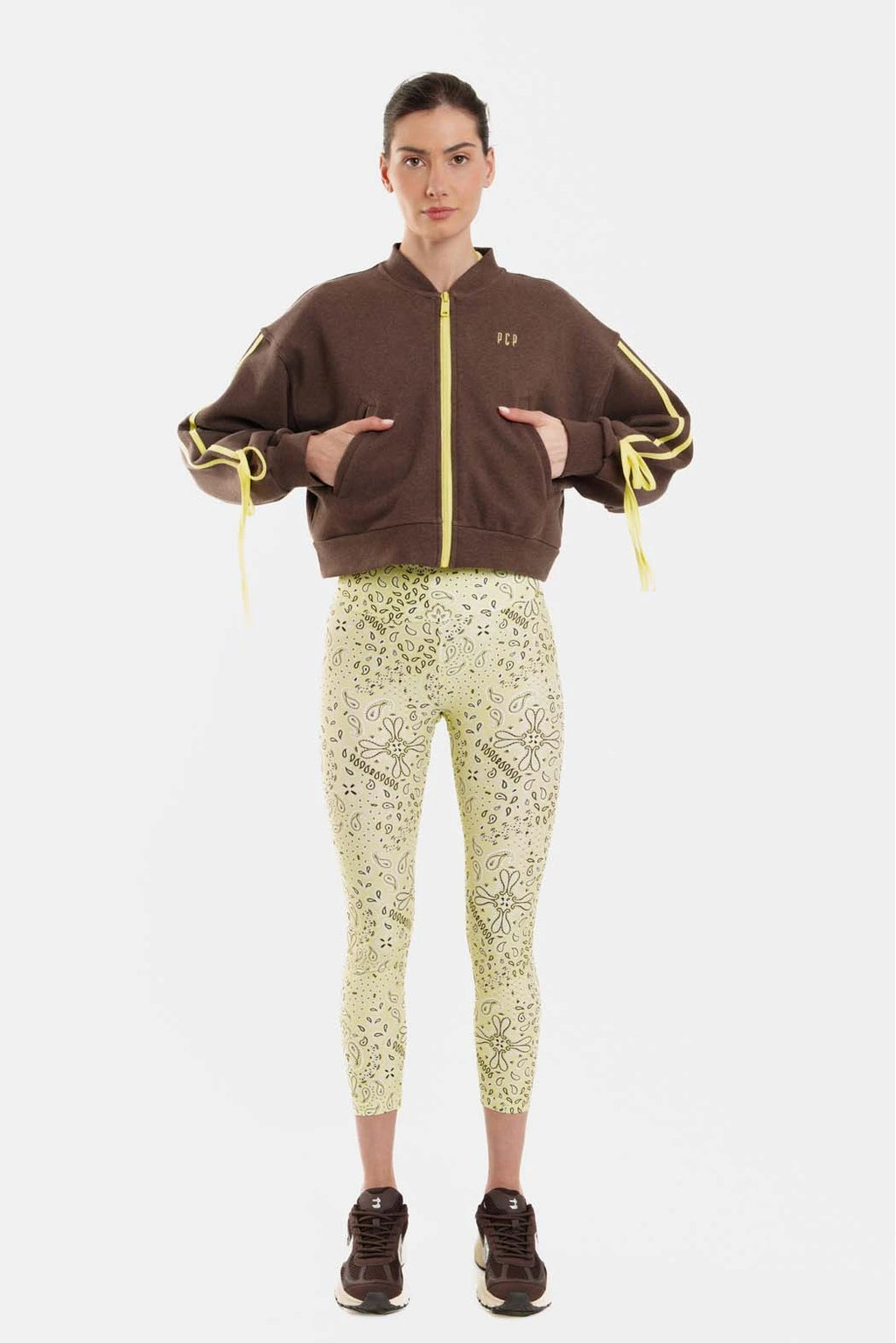 Person wearing a brown jacket with yellow accents and light green patterned pants on a white background
