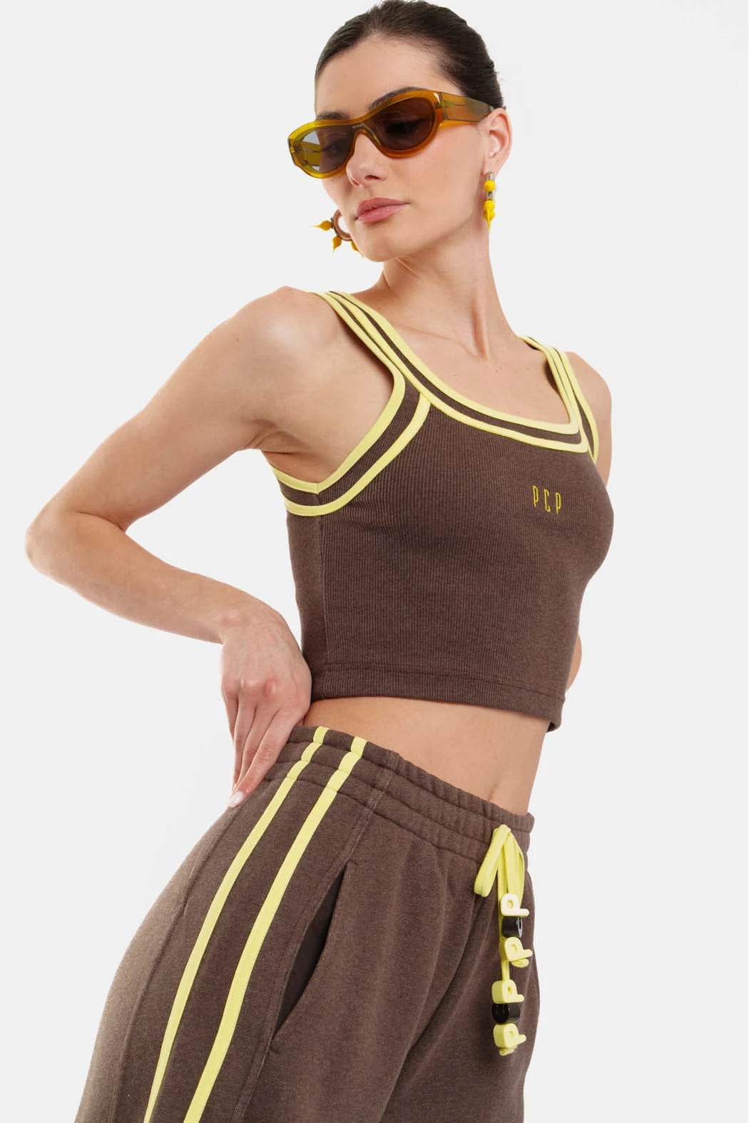 Woman wearing a brown crop top and pants with yellow accents on a white background