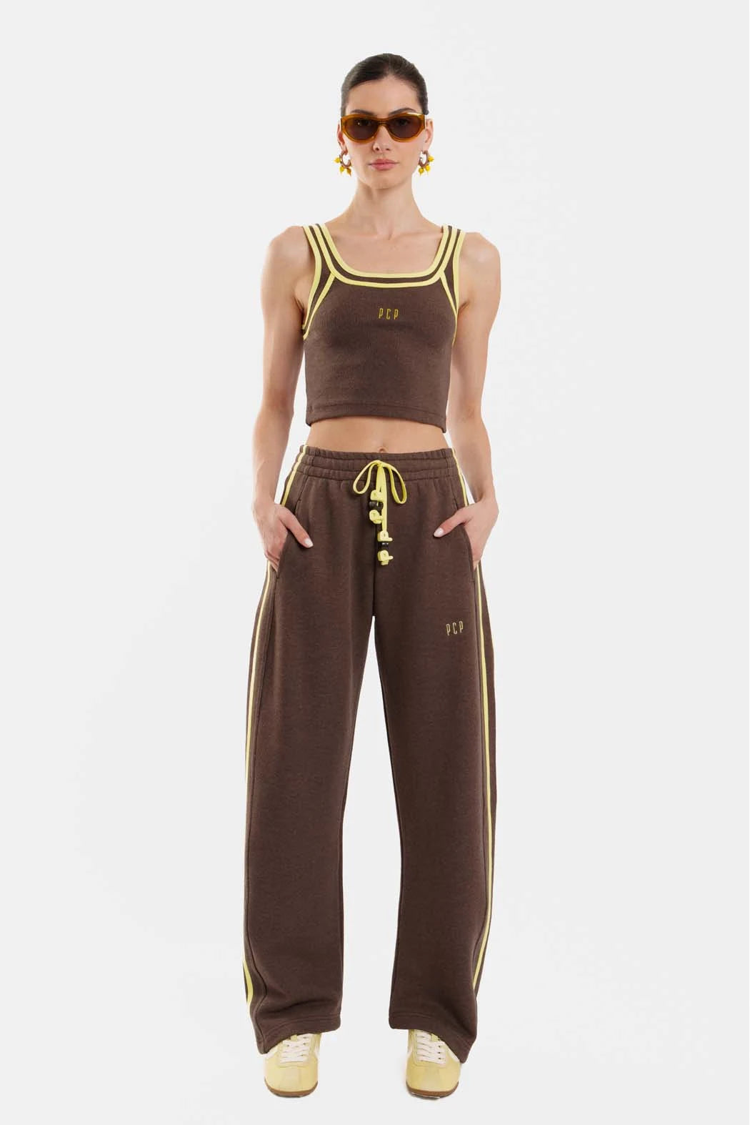 Woman wearing a brown sports outfit with yellow accents on a white background