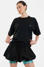 Woman wearing a black oversized t-shirt and black shorts with floral leggings on a white background