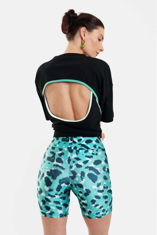 Woman wearing a black open-back top and green leopard print shorts on a white background