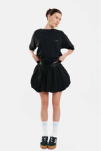 Person wearing a black t-shirt and skirt with white socks and black shoes on a white background