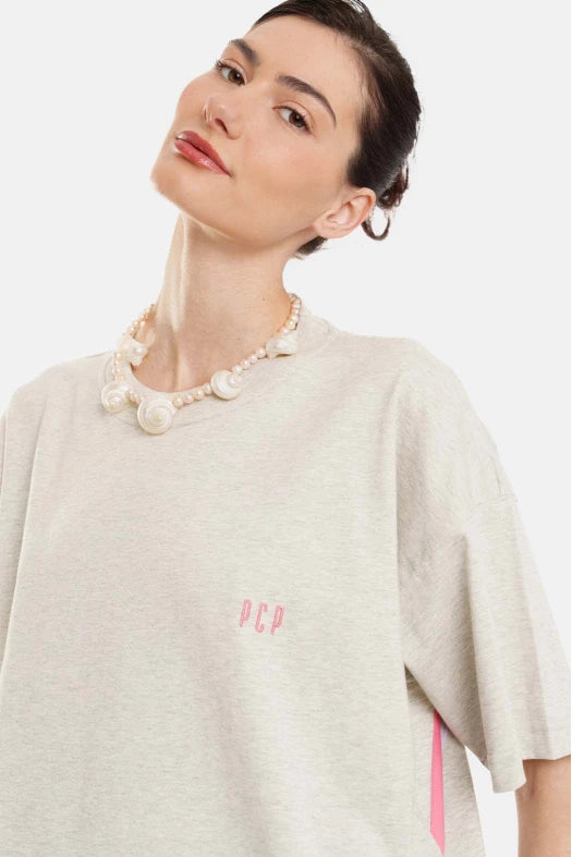 Woman wearing a light-colored top with a logo and a pearl necklace on a white background