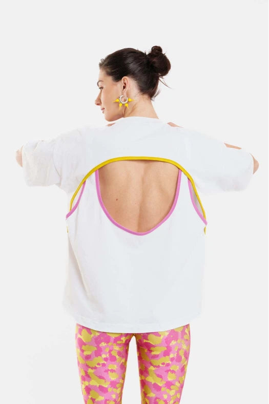 Woman wearing a white open-back top with pink trim and colorful leggings on a white background