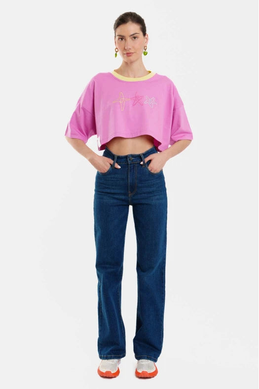 Person wearing a pink cropped top with graphics and blue jeans on a white background