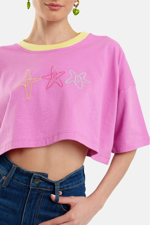 Person wearing a pink crop top with colorful star designs and blue jeans on a white background