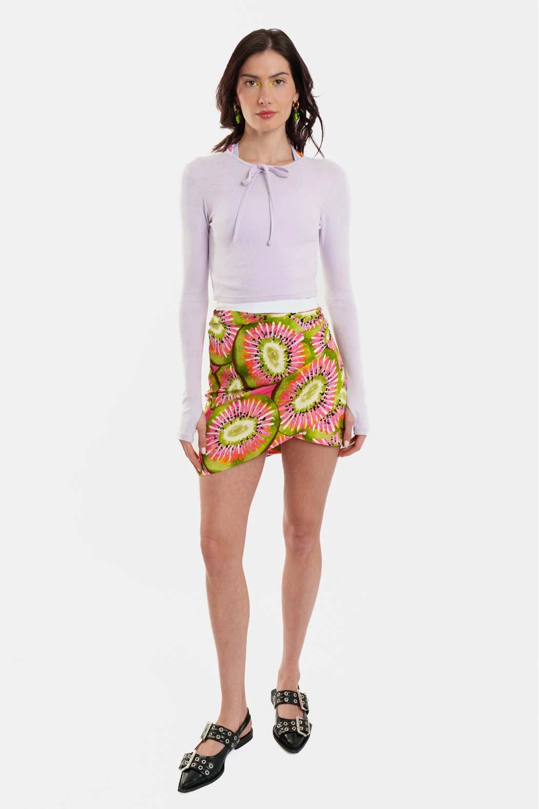 Woman wearing a light purple top and colorful floral skirt on a white background