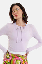 Woman wearing a light purple long-sleeve top with a tie detail and colorful tie-dye pants on a white background