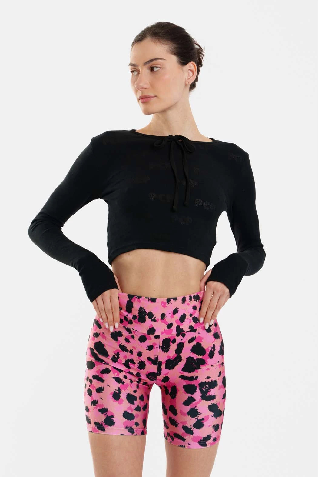 Woman wearing a black long-sleeve crop top and pink leopard print shorts on a white background