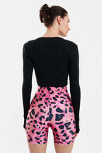 Person wearing a black long-sleeve top and pink leopard print shorts on a white background