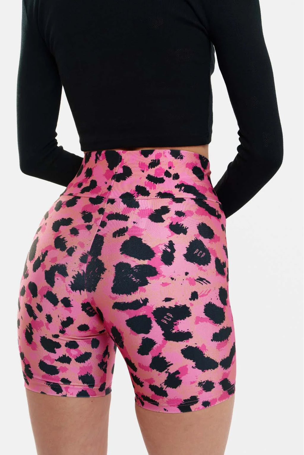 Person wearing pink leopard print shorts with a black long-sleeve top on a white background