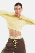 Woman wearing a yellow cropped top and brown pants with a white background