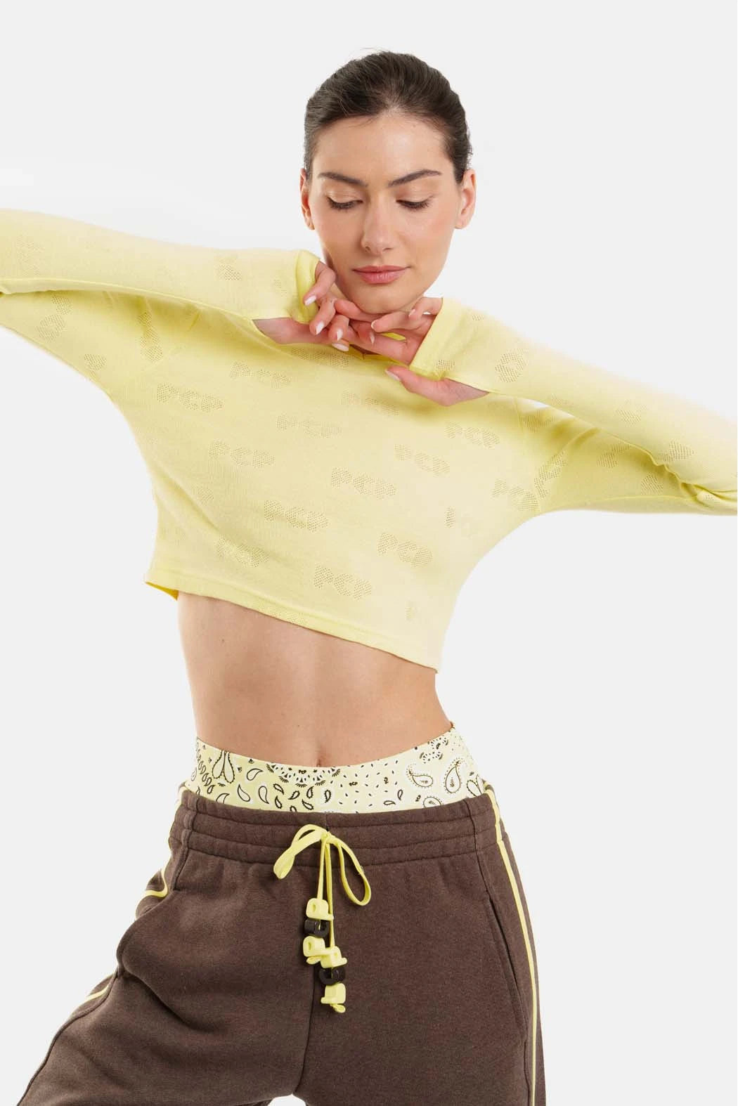 Woman wearing a yellow cropped top and brown pants with a white background