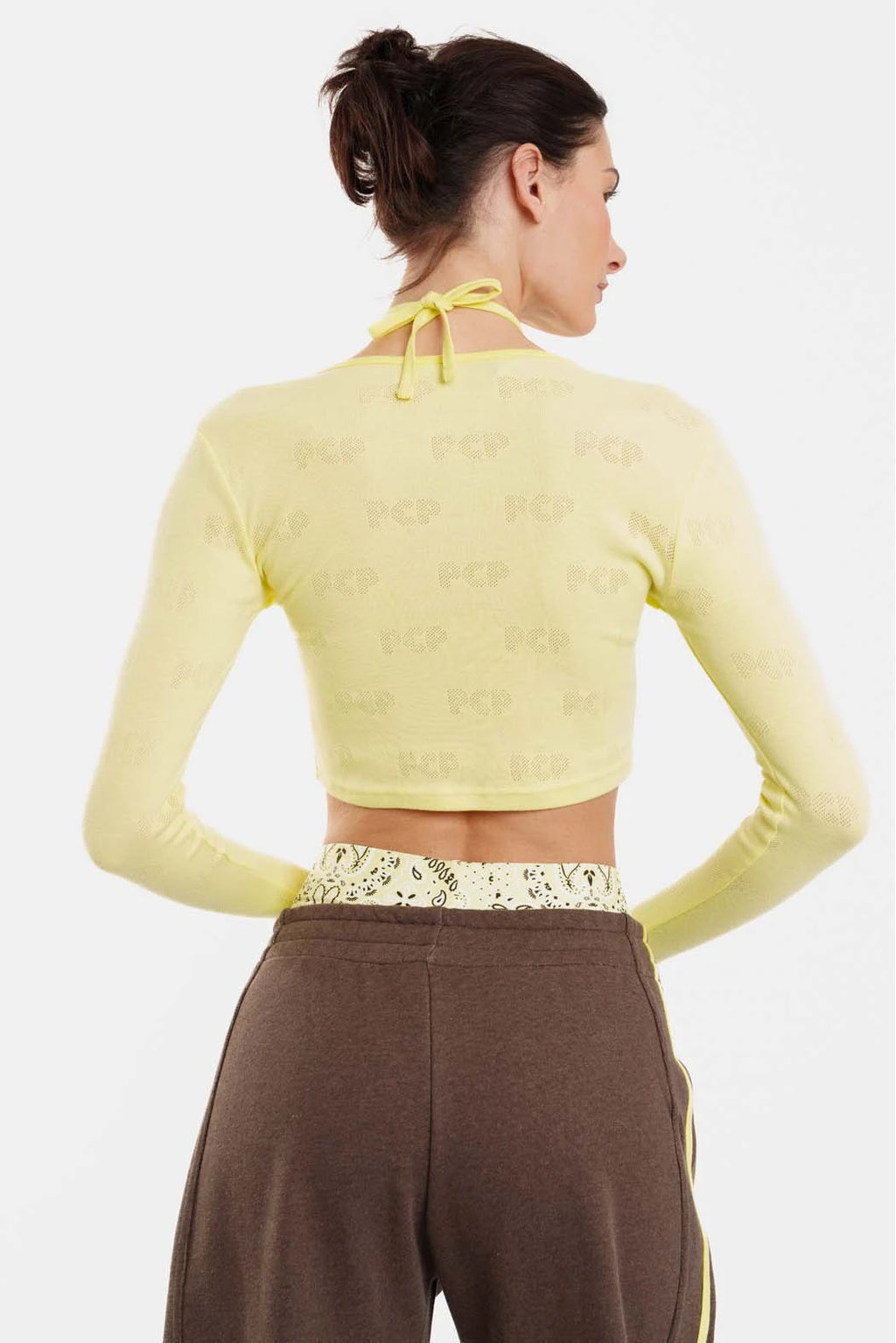 Woman wearing a yellow long-sleeve crop top and brown pants on a white background