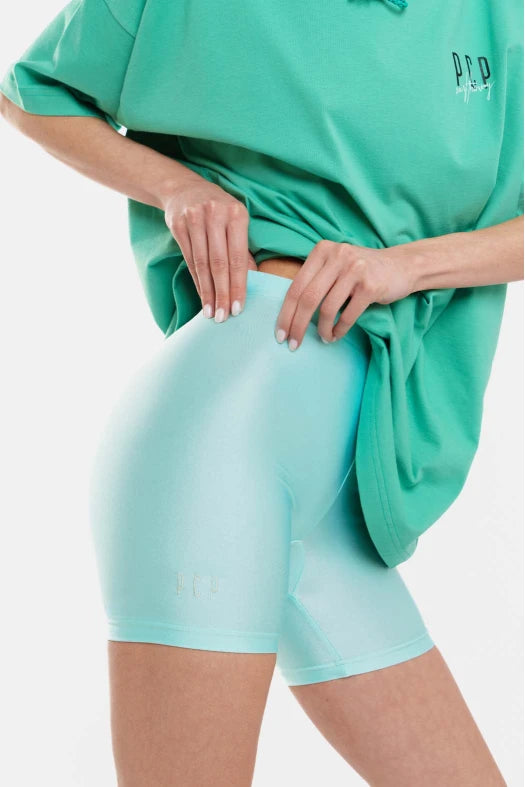 Person wearing a green oversized shirt and light blue shorts on a white background