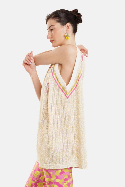 Woman wearing a beige patterned top with a V-neckline and colorful pants on a white background