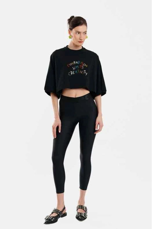 Person wearing a black oversized shirt with colorful text and black leggings on a white background