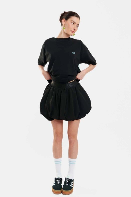 Person wearing a black t-shirt and skirt with white socks and black shoes on a white background