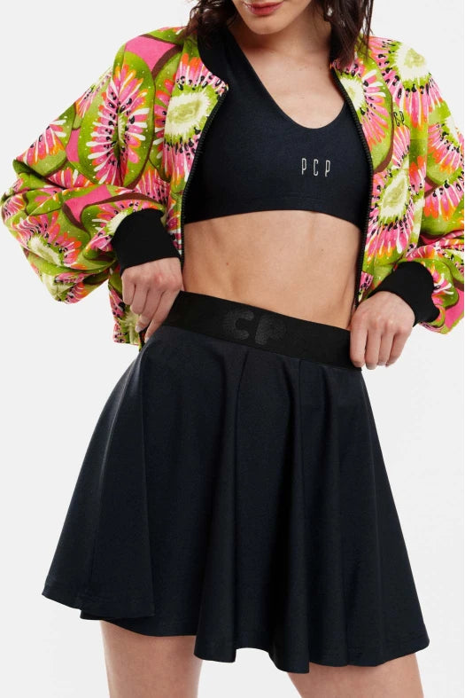 Person wearing a colorful jacket, black sports bra, and black skirt on a white background