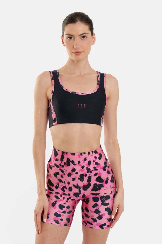 Woman wearing a black sports bra and pink leopard print leggings on a white background