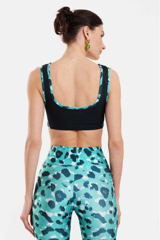 Woman wearing a black sports bra and teal patterned leggings on a white background