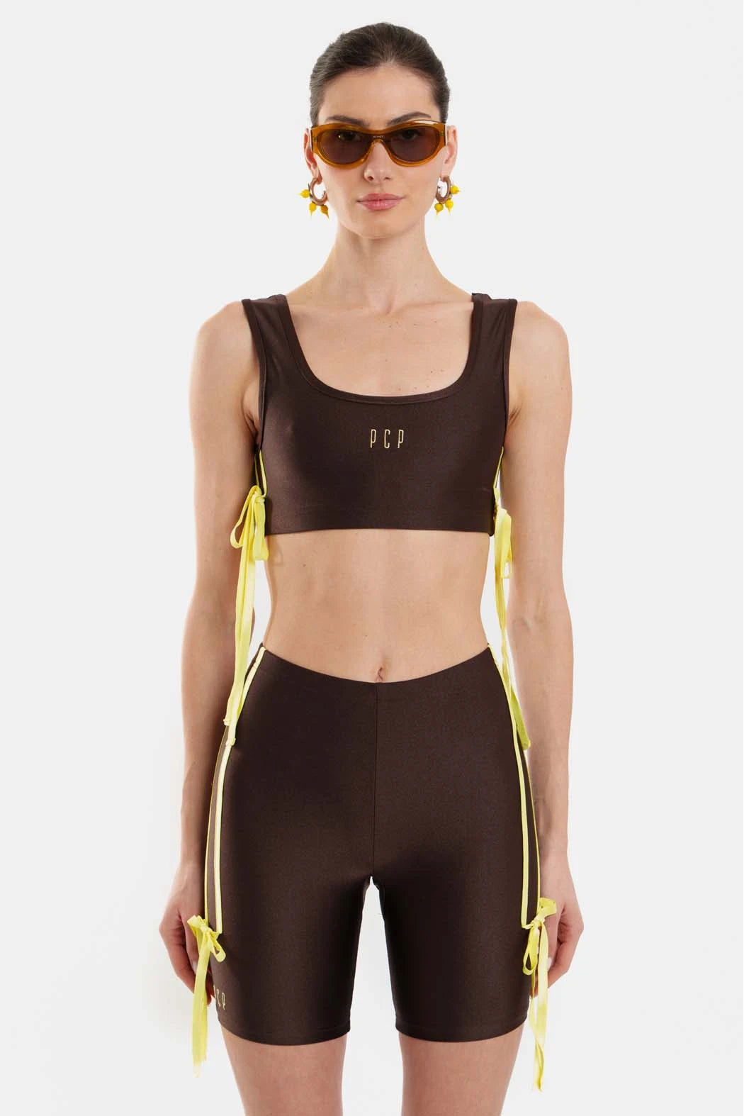 Woman wearing a brown sports outfit with yellow accents on a white background