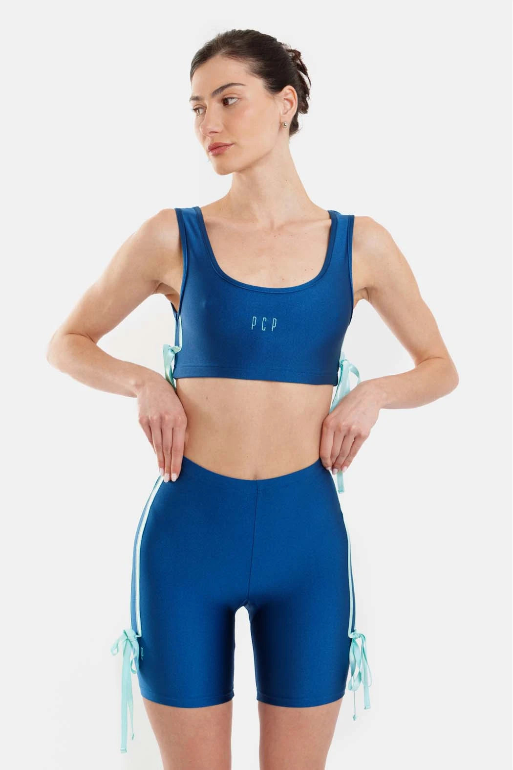 Woman wearing a blue athletic outfit with a sports bra and shorts on a white background