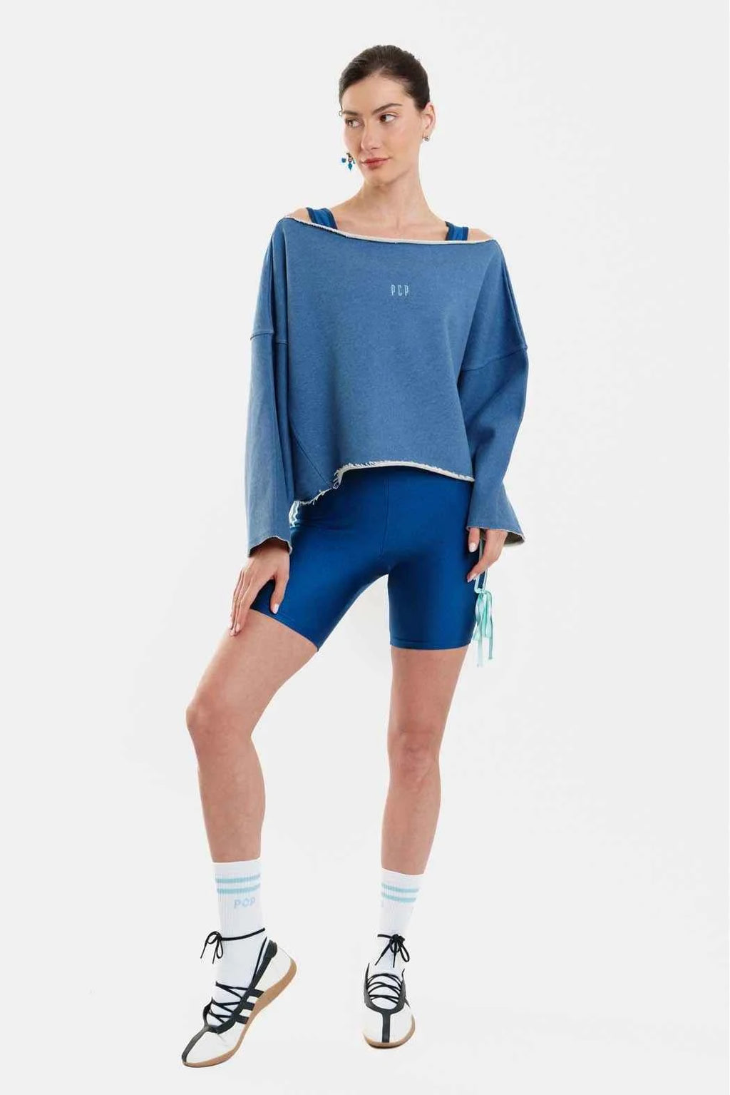 Woman wearing a blue oversized sweatshirt, blue shorts, and black sneakers on a white background