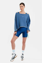 Woman wearing a blue oversized sweatshirt, blue shorts, and black sneakers on a white background