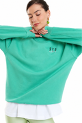 A woman wearing a mint green oversized sweatshirt with a small white 'PCP.