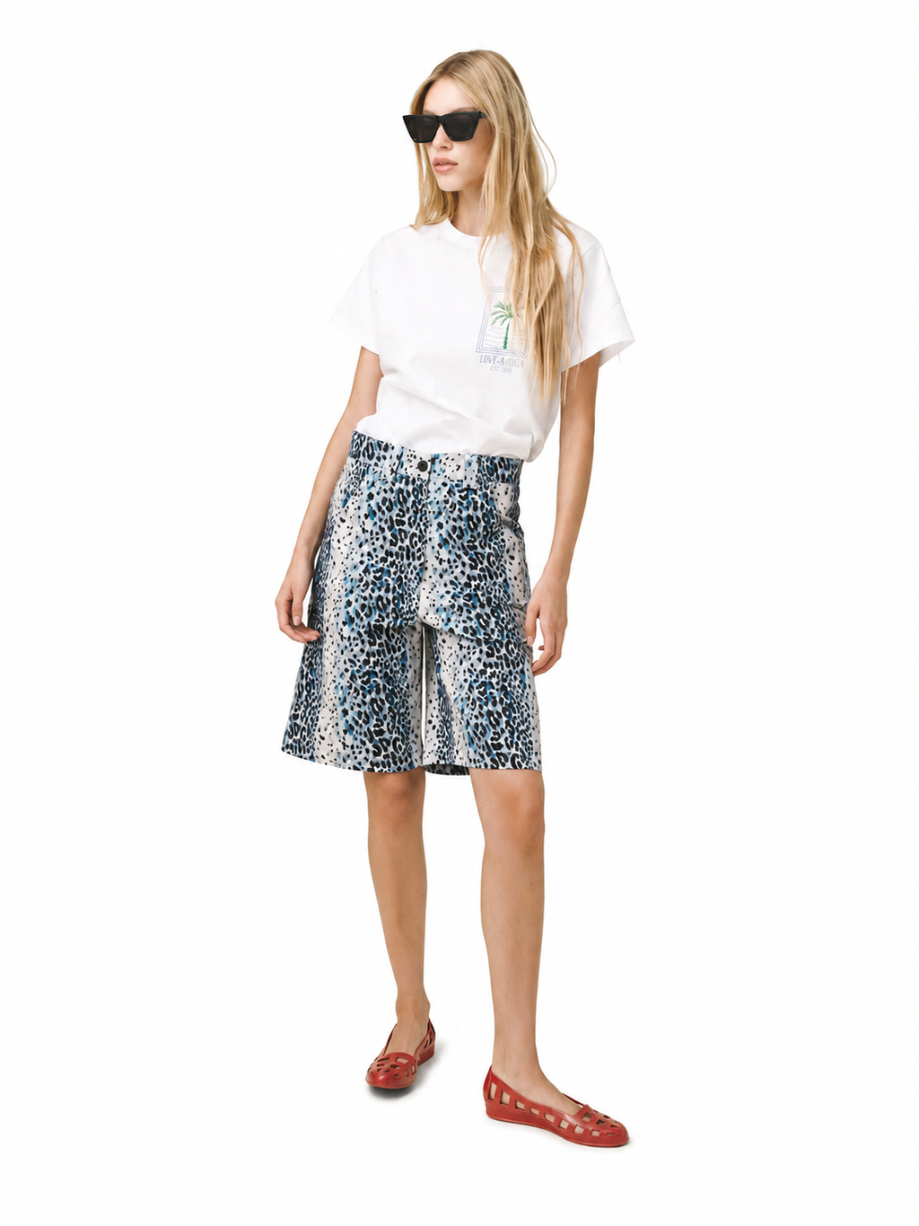 A woman modeling a white graphic t-shirt, a blue and white leopard-print wrap skirt, and red flat shoes against a plain white background.