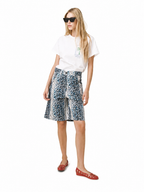 A woman modeling a white graphic t-shirt, a blue and white leopard-print wrap skirt, and red flat shoes against a plain white background.