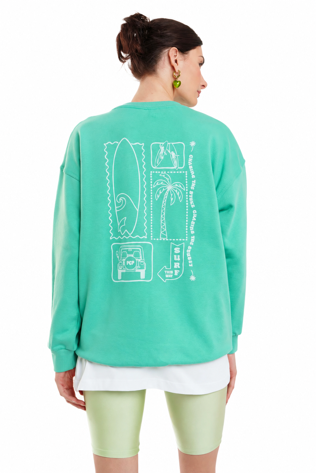 A woman shown from the back wearing a mint green crewneck sweatshirt with a white graphic print on the back, paired with light green biker shorts and a white undershirt, against a plain white background.