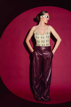 Woman wearing a patterned top and purple pants against a pink background