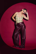 Person wearing a patterned top and shiny purple pants against a pink background