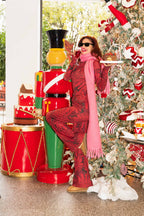 Woman in red patterned outfit and pink scarf standing next to a decorated Christmas tree with a large nutcracker and cake display.
