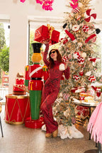 Person in red outfit with oversized shoes near a decorated Christmas tree