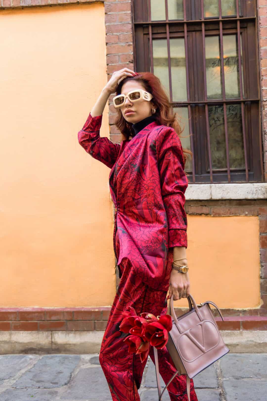 Woman in a red outfit with a pink handbag standing against a brick wall.