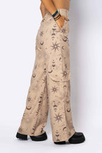 Beige pants with celestial pattern worn by a person on a white background