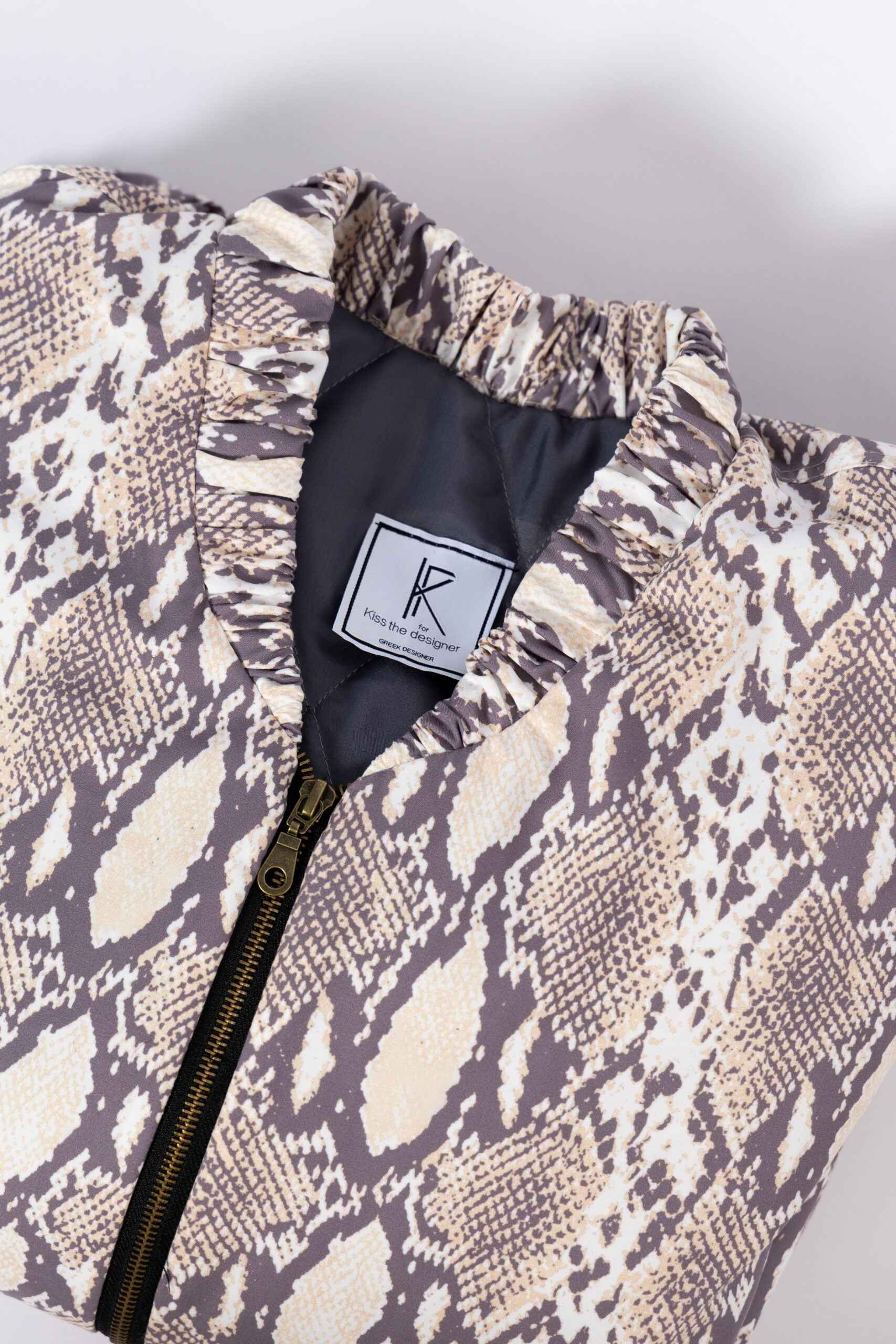 Partial view of a snake-print jacket with a black zipper and a "Kiss the Designer" tag.