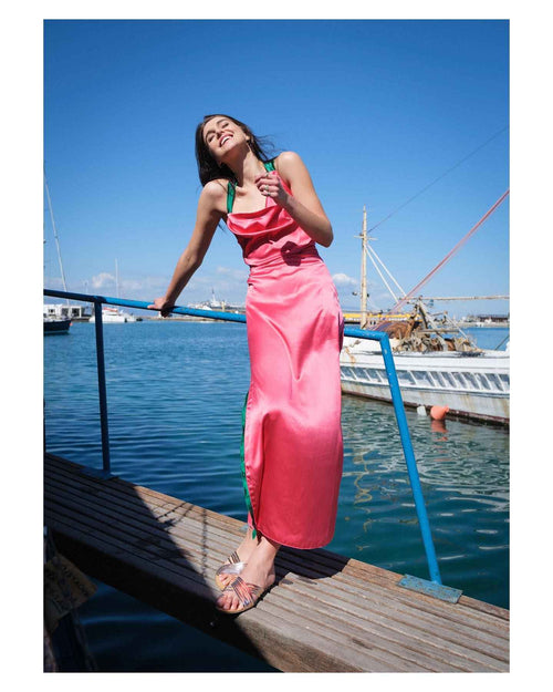 Woman in a pink dress standing on a dock by the water with clear blue skies.