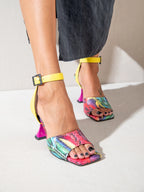 Colorful snake print high-heeled shoes with yellow straps on a neutral background